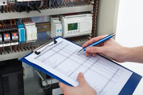 Electrician Holding Clipboard While Examining Fusebox.