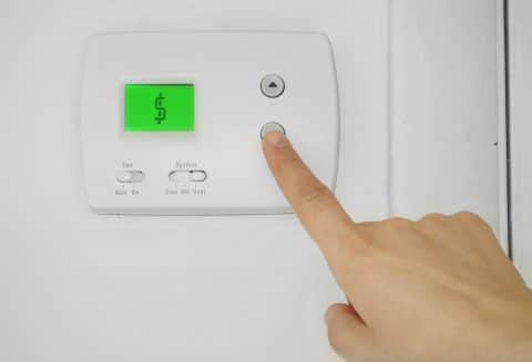 Person adjusting a wall thermostat with dollar sign symbol on the display
